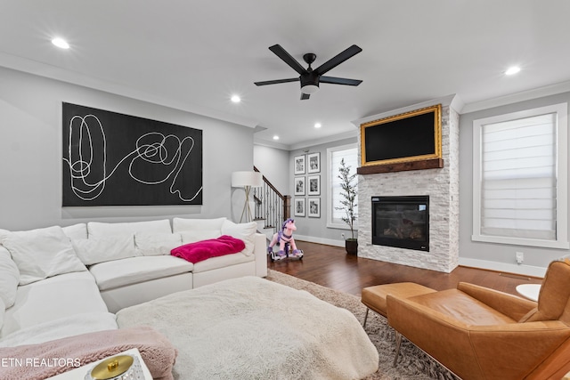 living area featuring baseboards, ceiling fan, ornamental molding, dark wood-type flooring, and a fireplace