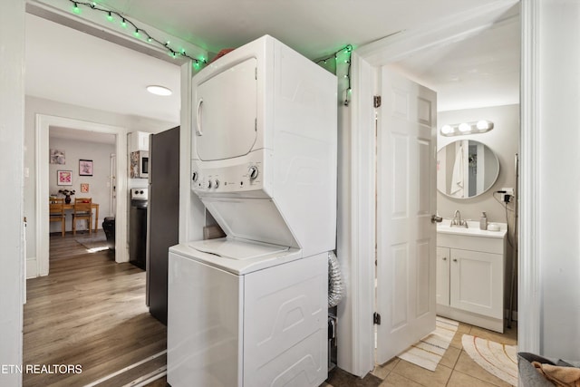 washroom with stacked washer and dryer, laundry area, a sink, and light tile patterned flooring