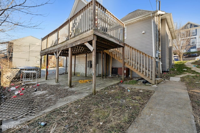 rear view of house with stairway, a deck, and roof with shingles