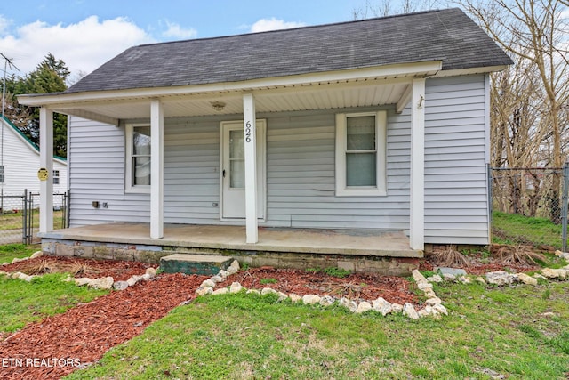 view of front facade featuring fence, covered porch, and roof with shingles