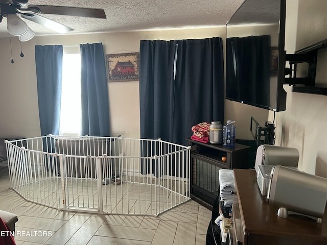 bedroom with a nursery area, ceiling fan, and a textured ceiling