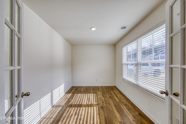 empty room with french doors, visible vents, a textured ceiling, wood finished floors, and baseboards