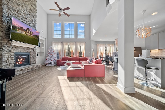 living room with ceiling fan, a stone fireplace, light hardwood / wood-style floors, and a towering ceiling