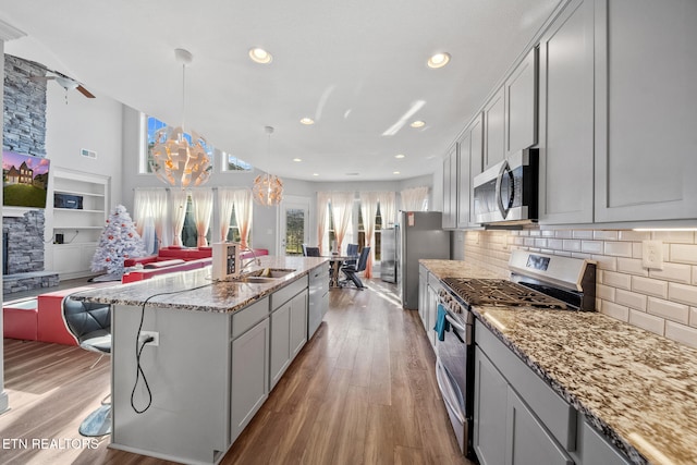 kitchen featuring hanging light fixtures, stainless steel appliances, light stone counters, light hardwood / wood-style floors, and an island with sink