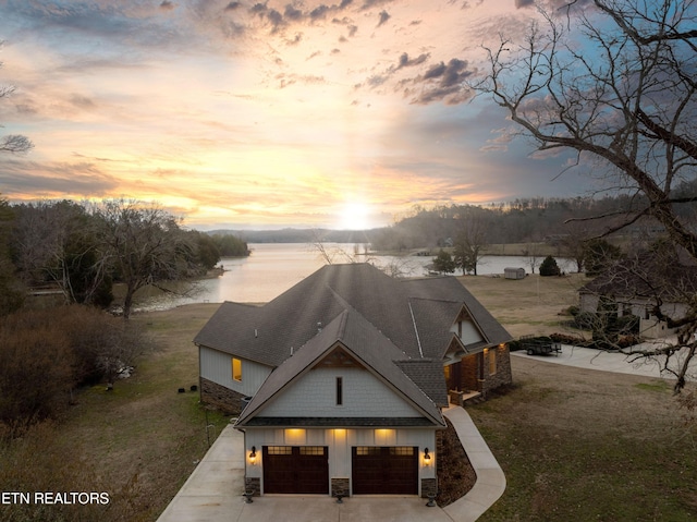 exterior space with a water view, stone siding, concrete driveway, a lawn, and board and batten siding