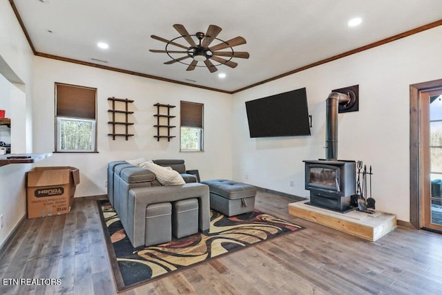 living room featuring crown molding, ceiling fan, hardwood / wood-style floors, and a wood stove