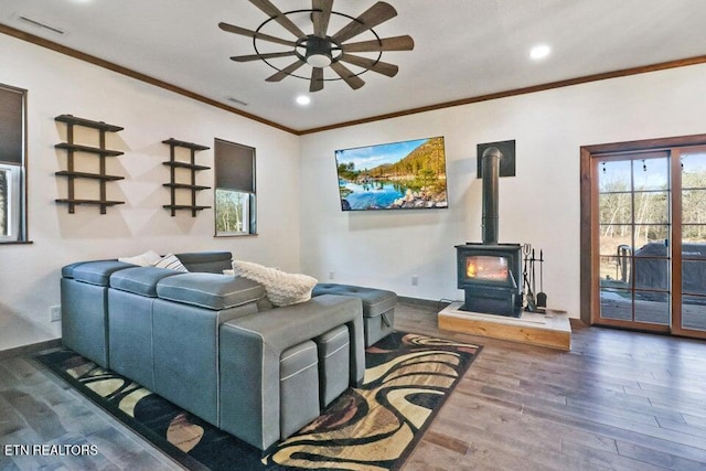 living room with ceiling fan, ornamental molding, dark hardwood / wood-style floors, and a wood stove