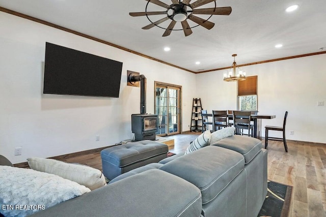 living room with crown molding, ceiling fan with notable chandelier, light hardwood / wood-style floors, and a wood stove