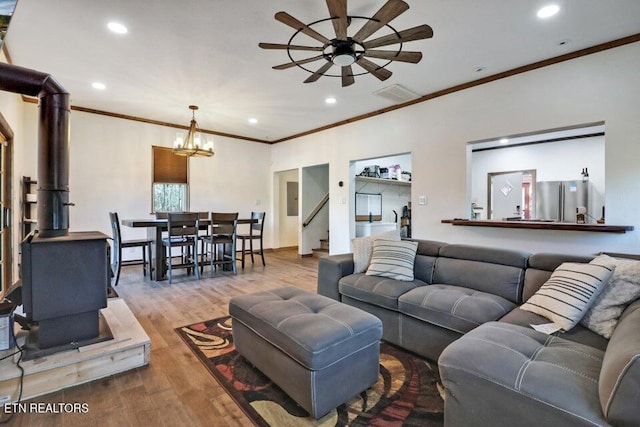 living room with ornamental molding, ceiling fan with notable chandelier, a wood stove, and hardwood / wood-style floors