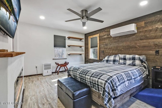 bedroom with a fireplace, wooden walls, a wall mounted AC, hardwood / wood-style flooring, and ceiling fan