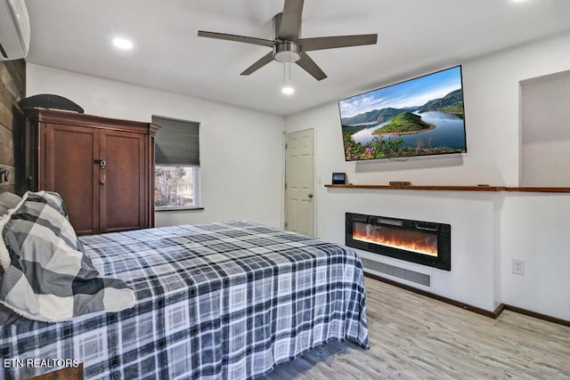 bedroom with ceiling fan, a wall unit AC, and light hardwood / wood-style flooring