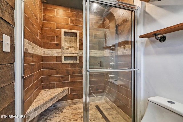 bathroom featuring a shower with door and toilet