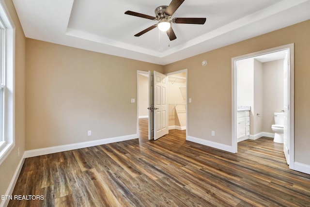 unfurnished bedroom featuring dark wood-type flooring, ceiling fan, ensuite bathroom, a raised ceiling, and a closet