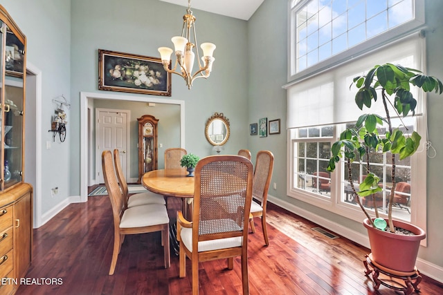 dining room featuring visible vents, baseboards, a towering ceiling, wood finished floors, and an inviting chandelier