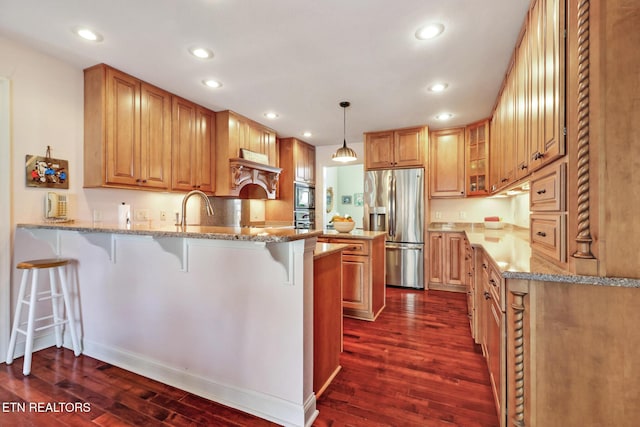 kitchen featuring a breakfast bar area, hanging light fixtures, appliances with stainless steel finishes, light stone countertops, and a peninsula