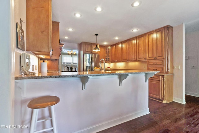 kitchen with stainless steel fridge with ice dispenser, glass insert cabinets, brown cabinets, a breakfast bar, and pendant lighting