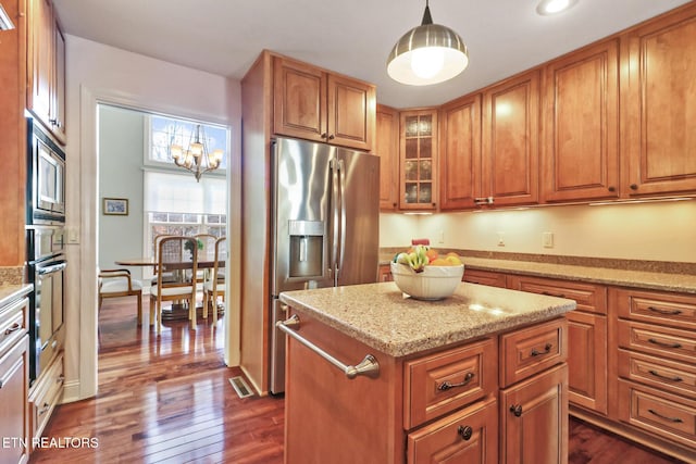 kitchen with a center island, brown cabinets, hanging light fixtures, glass insert cabinets, and light stone countertops