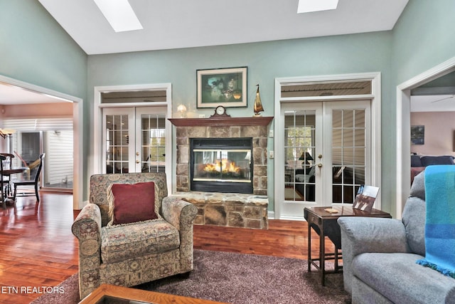 living room with a stone fireplace, french doors, a skylight, and wood finished floors