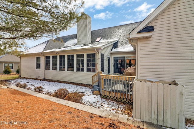 snow covered rear of property featuring a shingled roof, a chimney, and a wooden deck