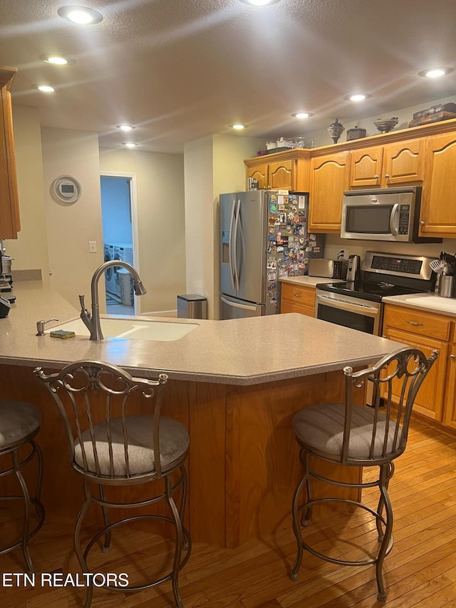 kitchen with sink, a kitchen bar, light hardwood / wood-style floors, and appliances with stainless steel finishes