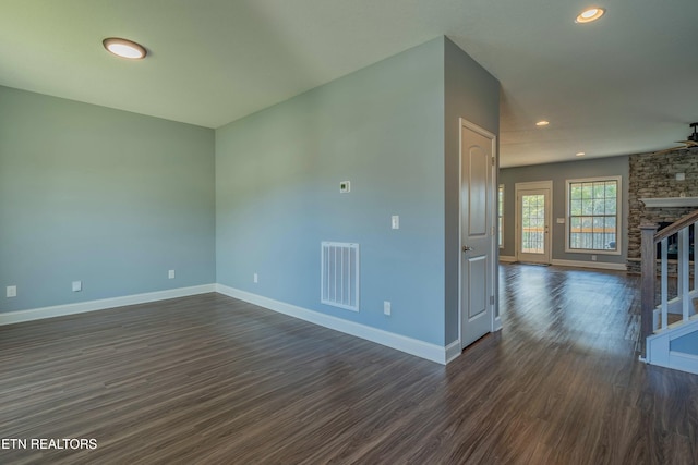 empty room with ceiling fan, dark hardwood / wood-style floors, and a stone fireplace