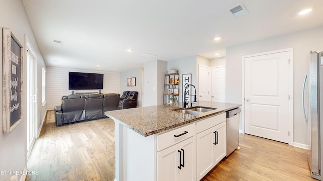 kitchen with sink, white cabinetry, light stone counters, appliances with stainless steel finishes, and a kitchen island with sink