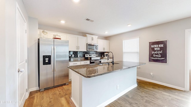 kitchen featuring sink, appliances with stainless steel finishes, white cabinetry, dark stone countertops, and an island with sink