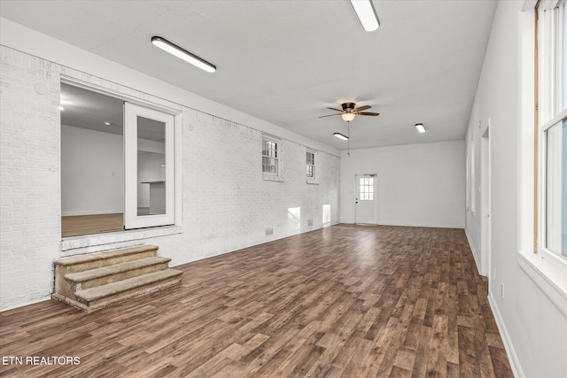 unfurnished living room with brick wall, dark hardwood / wood-style floors, and ceiling fan