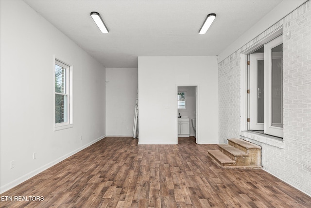 unfurnished room with dark wood-type flooring and brick wall