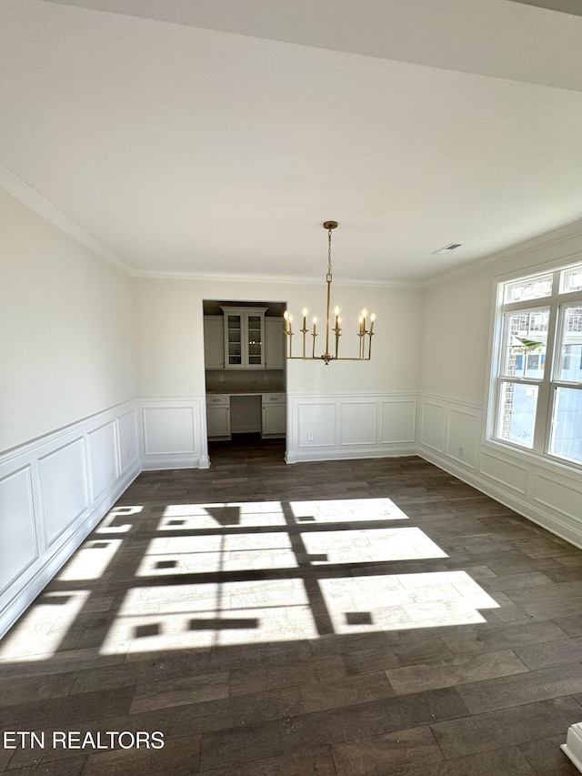 unfurnished dining area featuring a decorative wall, a notable chandelier, crown molding, and dark wood-type flooring