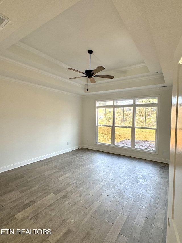 empty room with dark wood finished floors, a raised ceiling, baseboards, and ornamental molding