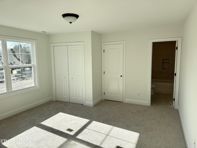 unfurnished bedroom with ensuite bath, carpet, baseboards, and a closet