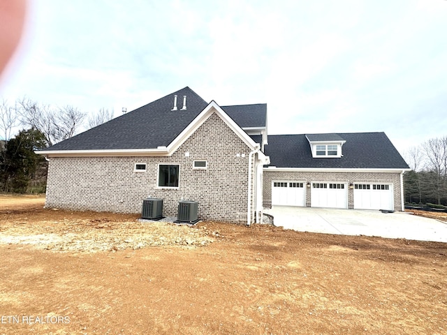 view of property exterior with brick siding, central AC unit, a garage, and roof with shingles