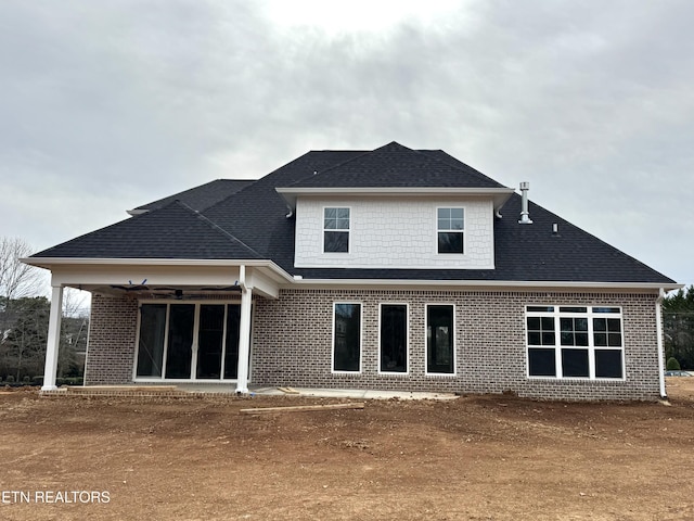 back of house featuring brick siding and roof with shingles