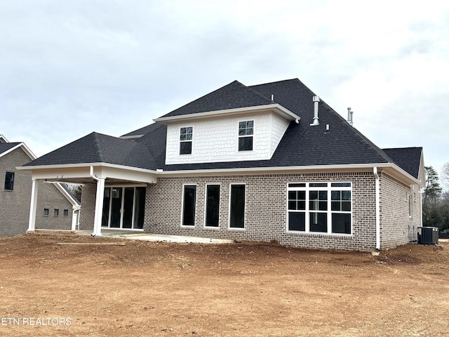 back of house featuring brick siding, central AC unit, and roof with shingles