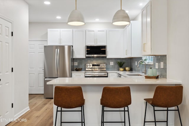 kitchen featuring appliances with stainless steel finishes, a breakfast bar, sink, white cabinets, and hanging light fixtures