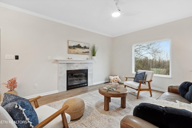 living room featuring a tiled fireplace, crown molding, ceiling fan, and light wood-type flooring