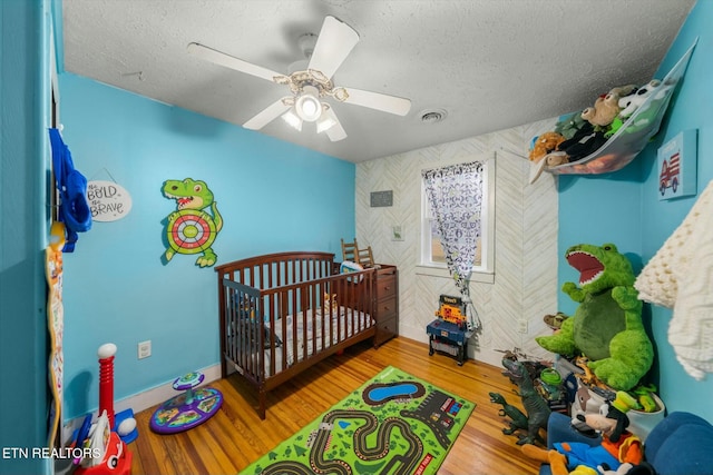 bedroom with a crib, ceiling fan, hardwood / wood-style floors, and a textured ceiling