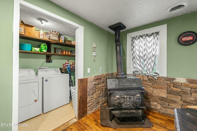 laundry area featuring hardwood / wood-style flooring, washer and clothes dryer, a textured ceiling, and a wood stove