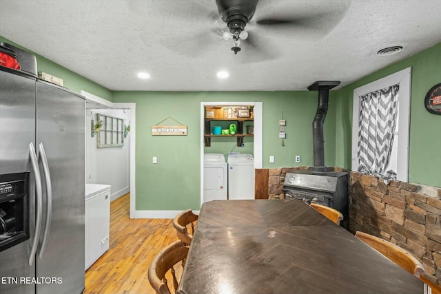 kitchen with stainless steel fridge with ice dispenser, a wood stove, ceiling fan, independent washer and dryer, and light wood-type flooring