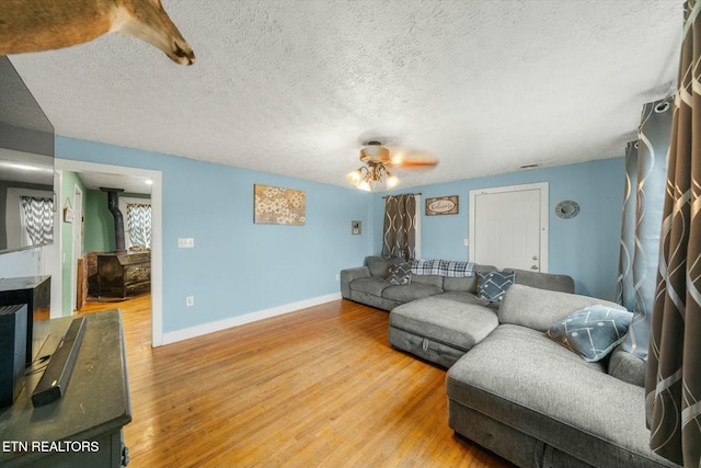 living room featuring ceiling fan, hardwood / wood-style floors, a textured ceiling, and a wood stove