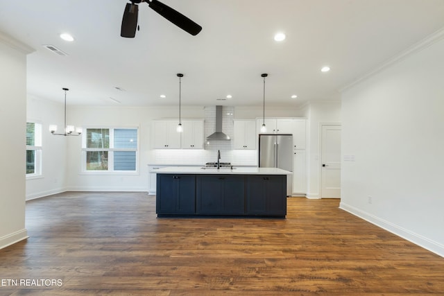 kitchen featuring a kitchen island with sink, visible vents, white cabinetry, wall chimney range hood, and freestanding refrigerator