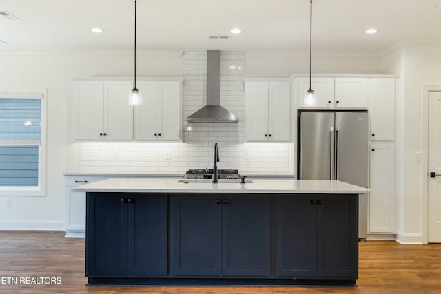 kitchen with wall chimney range hood, stainless steel appliances, white cabinets, and wood finished floors