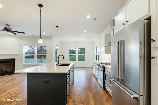 kitchen with a center island with sink, high end appliances, decorative backsplash, a sink, and wood finished floors