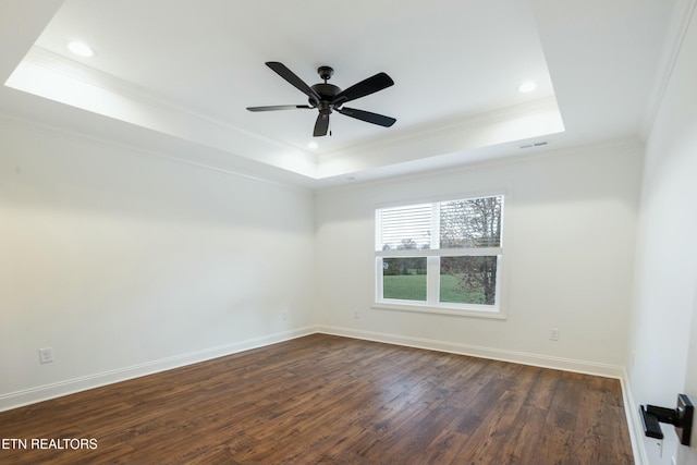 empty room featuring ornamental molding, a tray ceiling, dark wood finished floors, and baseboards