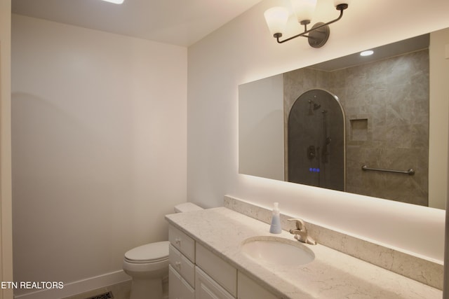 bathroom with a tile shower, vanity, toilet, and baseboards
