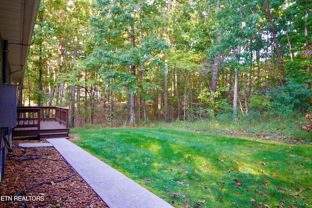 view of green lawn featuring a wooden deck and a forest view