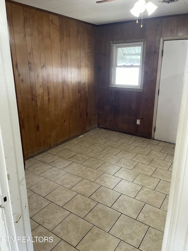 tiled empty room featuring ceiling fan and wooden walls