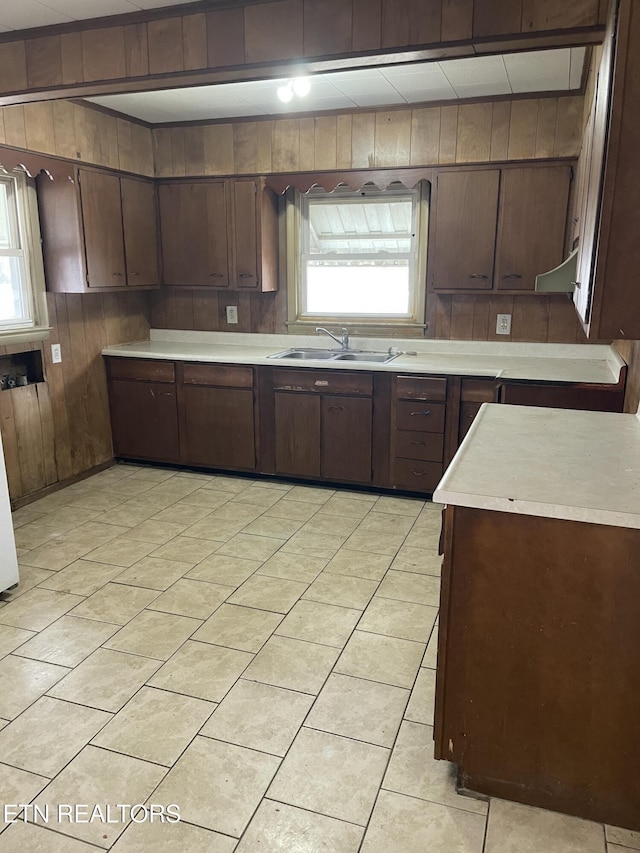 kitchen featuring sink, wooden walls, dark brown cabinetry, and light tile patterned floors