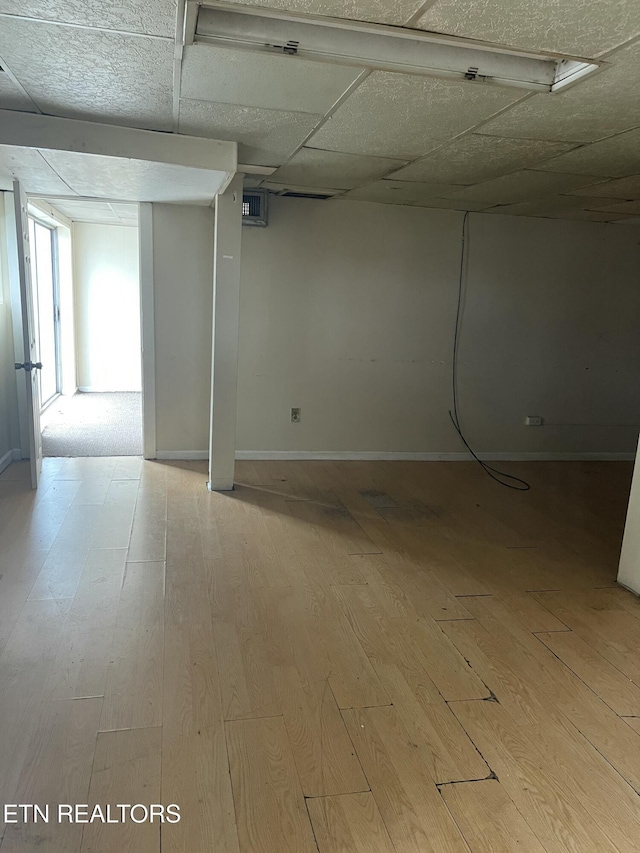 basement featuring a drop ceiling and light hardwood / wood-style flooring